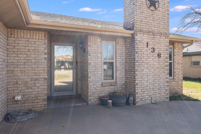 doorway to property featuring brick siding, a shingled roof, and a chimney