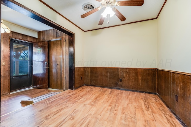 unfurnished room with crown molding, wood walls, visible vents, and a wainscoted wall