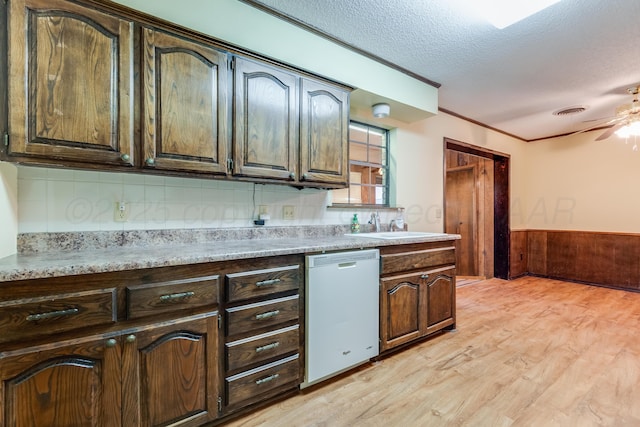 kitchen featuring light wood-style flooring, a textured ceiling, light countertops, a wainscoted wall, and white dishwasher