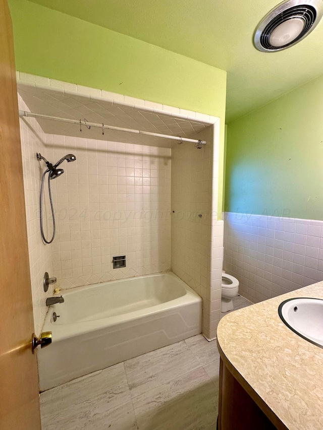 full bathroom featuring toilet, tiled shower / bath combo, vanity, and tile walls