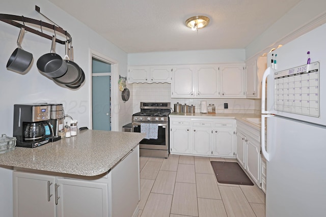 2901 Carter St, Amarillo, TX 79103 - kitchen with stainless steel range with gas cooktop, freestanding refrigerator, decorative backsplash, white cabinetry, and light countertops