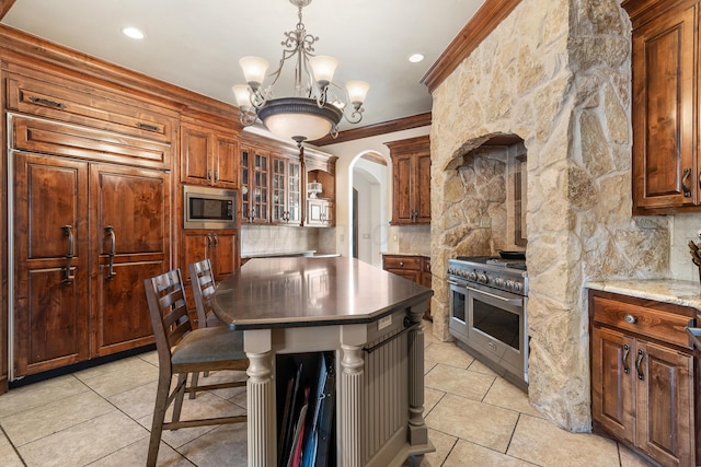 kitchen featuring crown molding, an inviting chandelier, light stone counters, decorative light fixtures, and stainless steel appliances