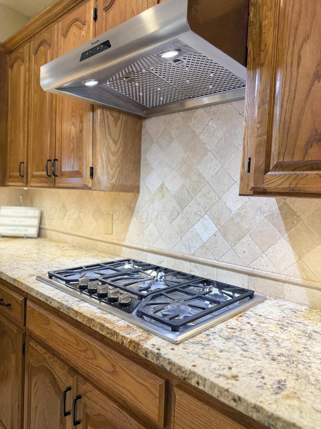 8 Glenbrook Dr, Borger, TX 79007 - kitchen with wall chimney range hood, stainless steel gas stovetop, brown cabinets, tasteful backsplash, and light stone countertops