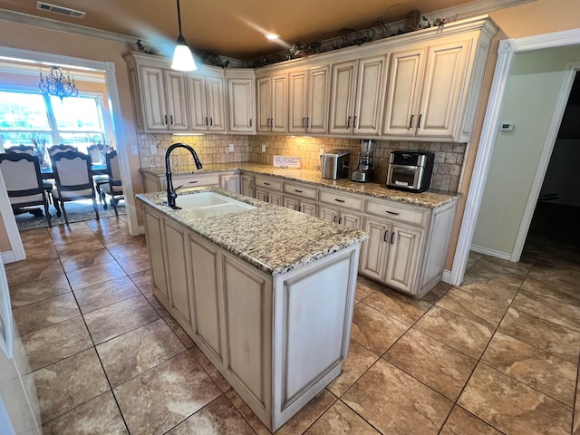 kitchen featuring sink, light stone counters, a chandelier, decorative light fixtures, and a kitchen island with sink