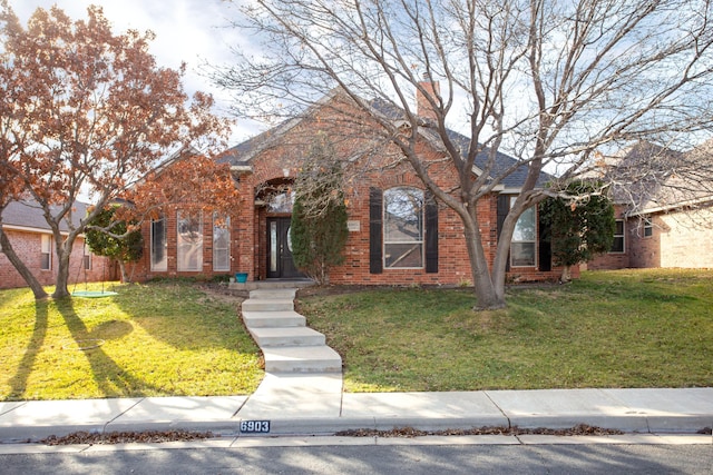 view of front facade featuring a chimney, a front lawn, and brick siding