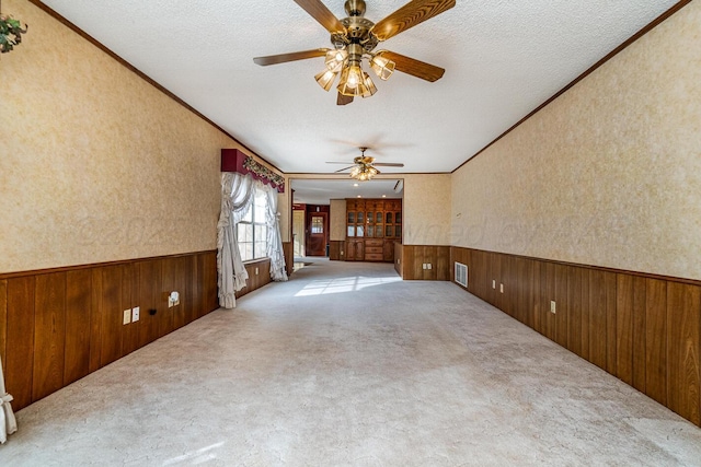 2723 County Road O, Friona, TX 79035 - carpeted empty room with a wainscoted wall, ceiling fan, wooden walls, ornamental molding, and a textured ceiling