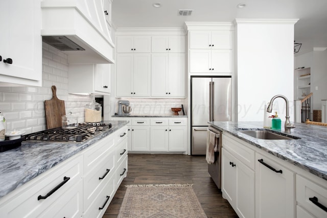 kitchen with white cabinetry, stainless steel appliances, custom range hood, light stone counters, and sink