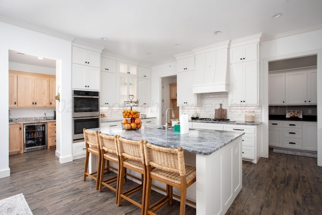 kitchen with light stone countertops, stainless steel double oven, an island with sink, wine cooler, and sink