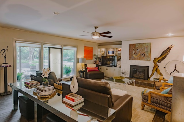 living area featuring a ceiling fan, a fireplace, wood finished floors, and ornamental molding