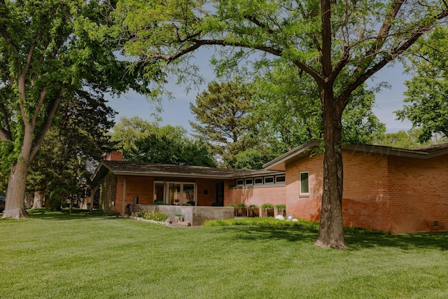 back of house featuring a chimney, a yard, and brick siding