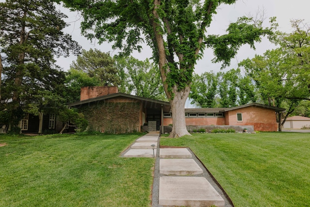 view of front of home featuring a front yard, a chimney, and brick siding
