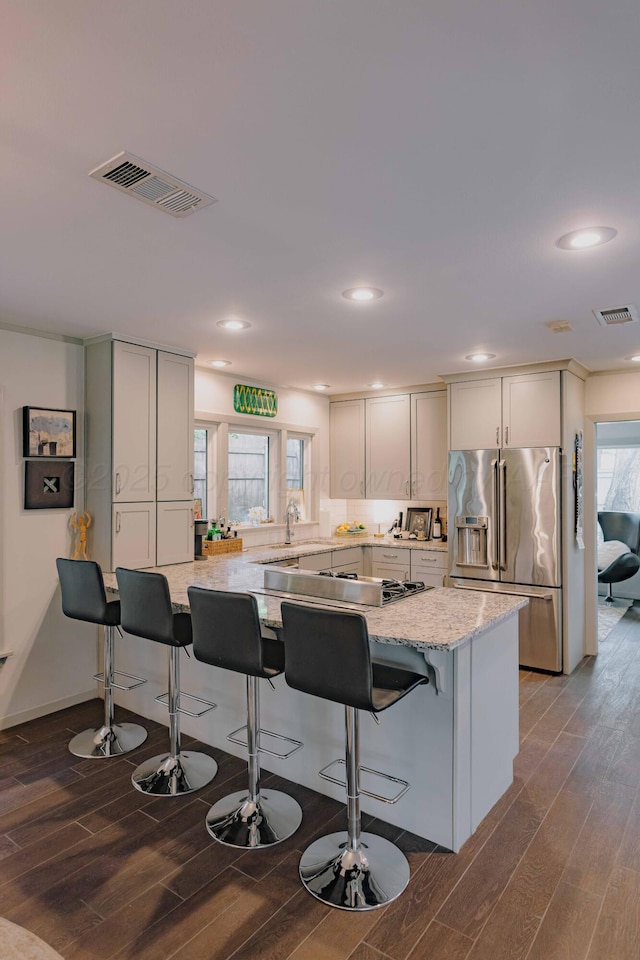 kitchen featuring stainless steel fridge with ice dispenser, dark wood-type flooring, light stone counters, a kitchen bar, and recessed lighting