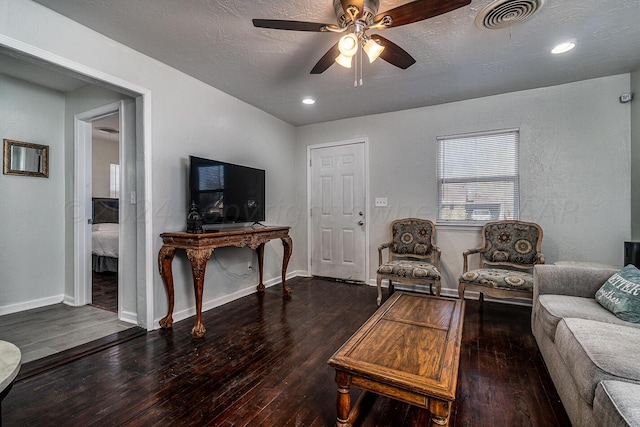 living room featuring ceiling fan, dark wood-type flooring, and a textured ceiling