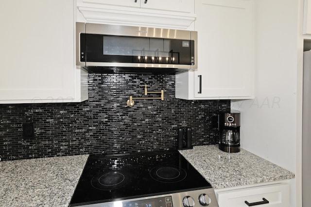 kitchen featuring decorative backsplash, range, white cabinetry, and light stone counters