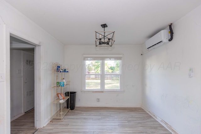 unfurnished dining area with a wall mounted air conditioner, light wood-style flooring, baseboards, and a chandelier