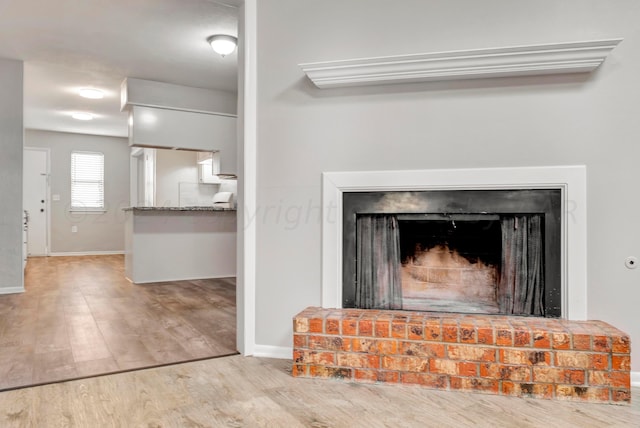 room details featuring baseboards, a fireplace with raised hearth, and wood finished floors