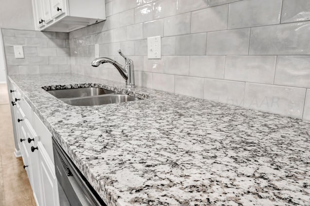 kitchen with decorative backsplash, white cabinets, a sink, light stone countertops, and dishwasher