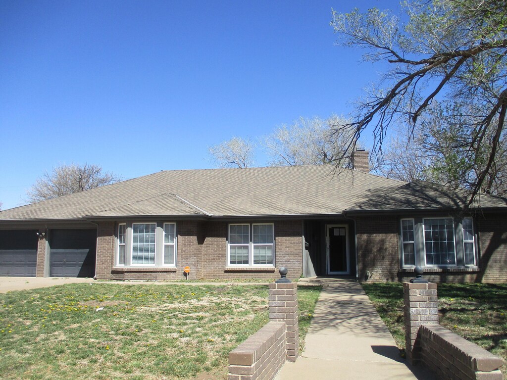 6702 Calumet Rd, Amarillo, TX 79106 - ranch-style home with an attached garage, a chimney, brick siding, a front lawn, and driveway