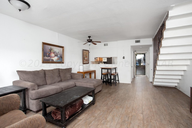 living room featuring a textured ceiling, light wood-type flooring, and ceiling fan