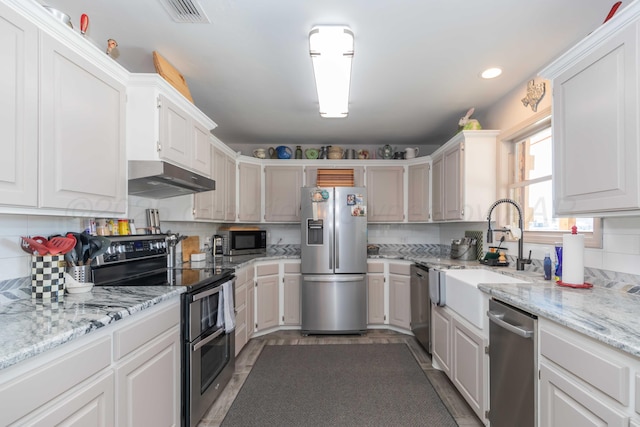 kitchen featuring stainless steel appliances, light stone countertops, decorative backsplash, sink, and white cabinetry