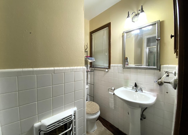 bathroom featuring heating unit, sink, tile walls, and toilet