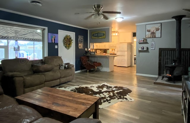 living room with ornamental molding, wood-type flooring, a wood stove, and ceiling fan