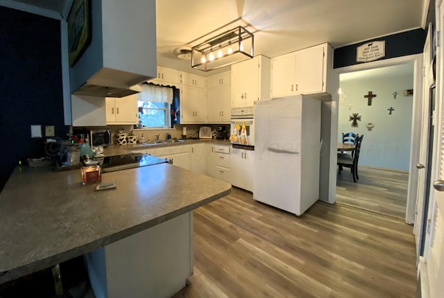 kitchen with sink, kitchen peninsula, white appliances, hardwood / wood-style floors, and white cabinets