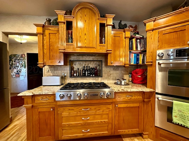 kitchen with stainless steel appliances, light stone countertops, light hardwood / wood-style flooring, and decorative backsplash