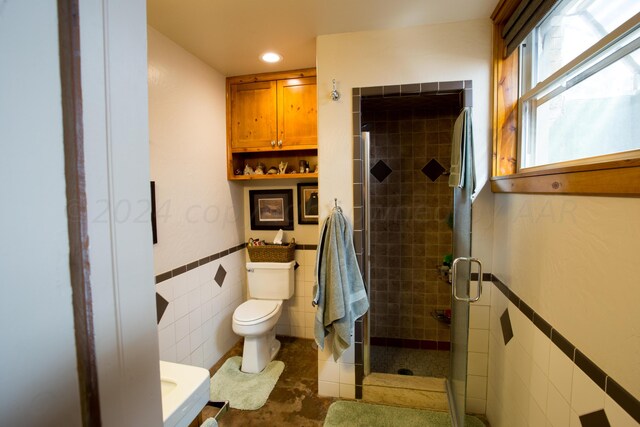 bathroom with a shower with door, toilet, and tile walls