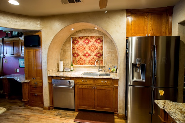 kitchen with sink, tasteful backsplash, stainless steel refrigerator with ice dispenser, light stone countertops, and light hardwood / wood-style flooring