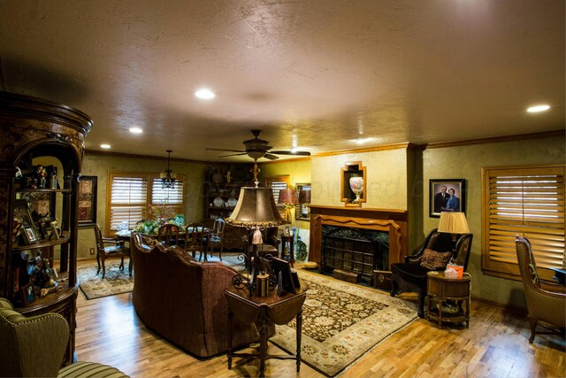 living room featuring a textured ceiling, hardwood / wood-style flooring, ornamental molding, ceiling fan, and a fireplace