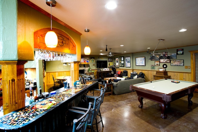 playroom featuring ceiling fan, concrete flooring, bar, wooden walls, and billiards