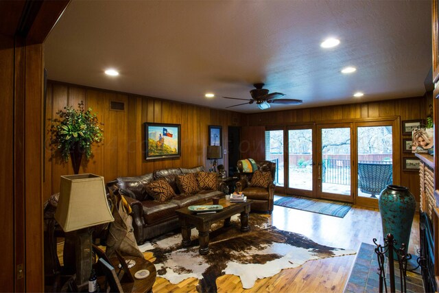 living room with french doors, light wood-type flooring, wooden walls, and ceiling fan