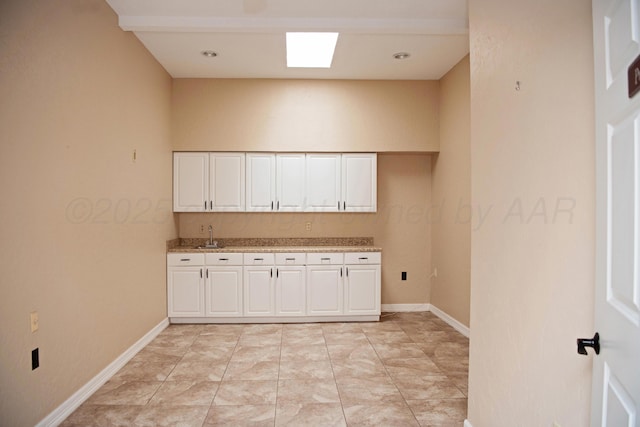 411 E 6th St, Hereford, TX 79045 - kitchen featuring white cabinets, a sink, baseboards, and light stone counters