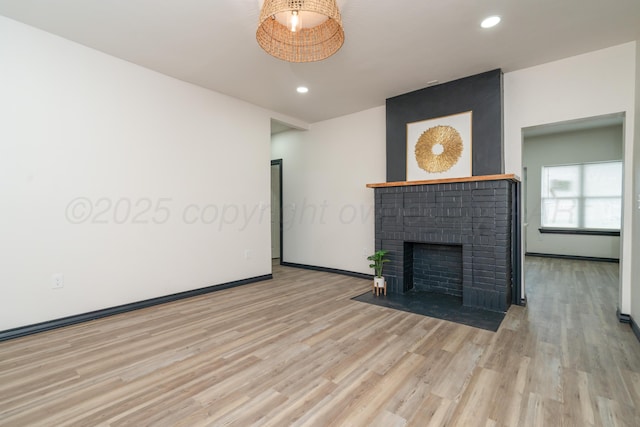 unfurnished living room featuring baseboards, recessed lighting, a brick fireplace, and wood finished floors