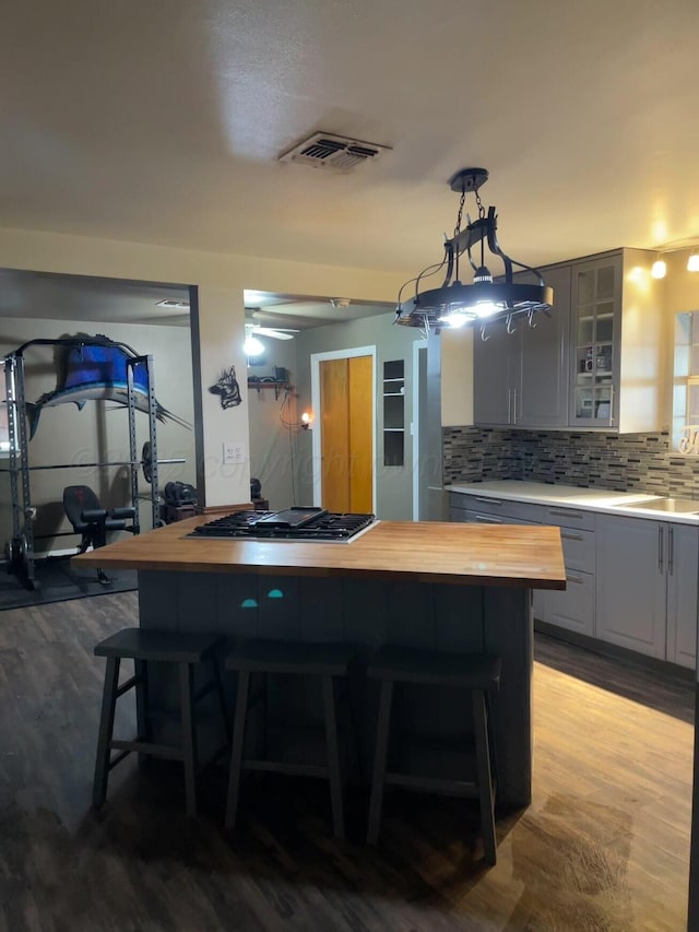 kitchen featuring glass insert cabinets, gas cooktop, wood counters, a breakfast bar area, and backsplash