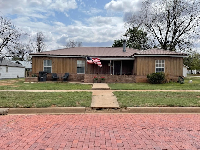 view of front of property featuring board and batten siding, metal roof, a front yard, and brick siding