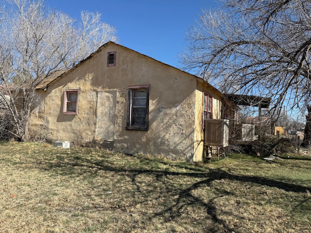 view of side of home with stucco siding, cooling unit, and a yard