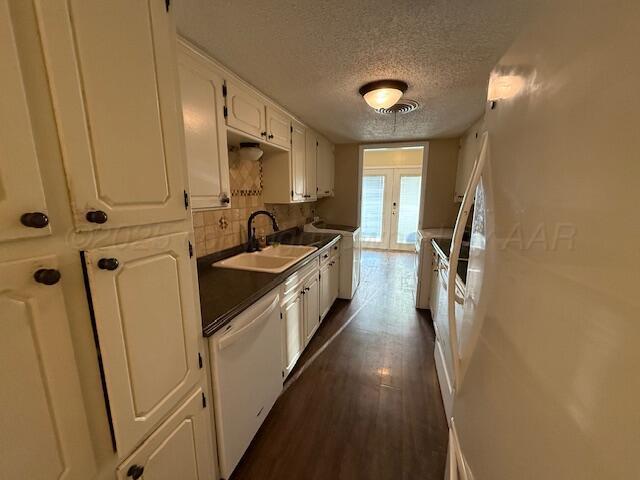 kitchen featuring a sink, backsplash, dark wood finished floors, white cabinets, and dishwasher