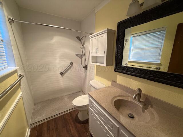 full bathroom featuring a tile shower, toilet, vanity, and wood finished floors