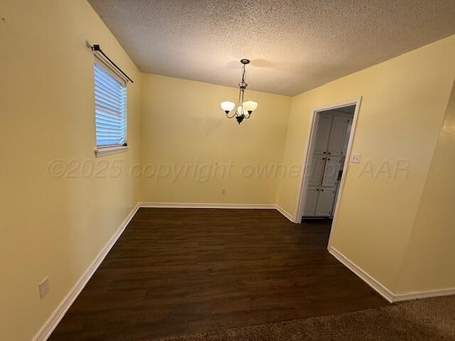 unfurnished room featuring a textured ceiling, dark wood-style floors, baseboards, and a chandelier