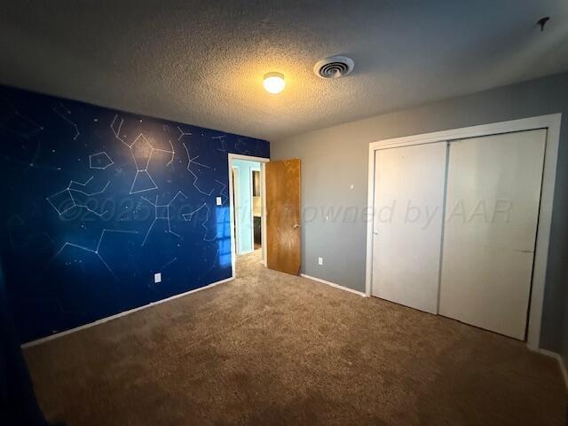 unfurnished bedroom with a closet, visible vents, a textured ceiling, and carpet floors