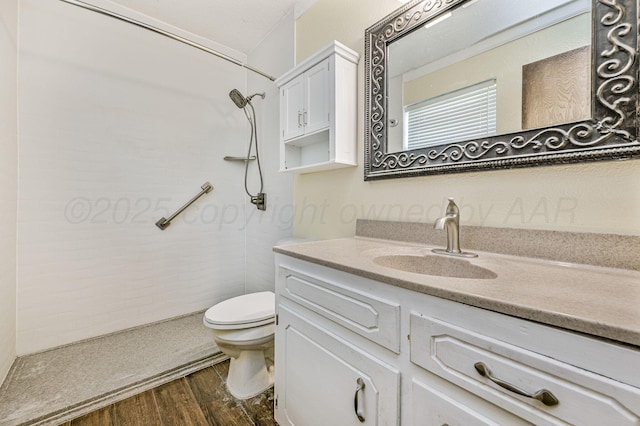 full bath featuring toilet, vanity, a tile shower, and wood finished floors