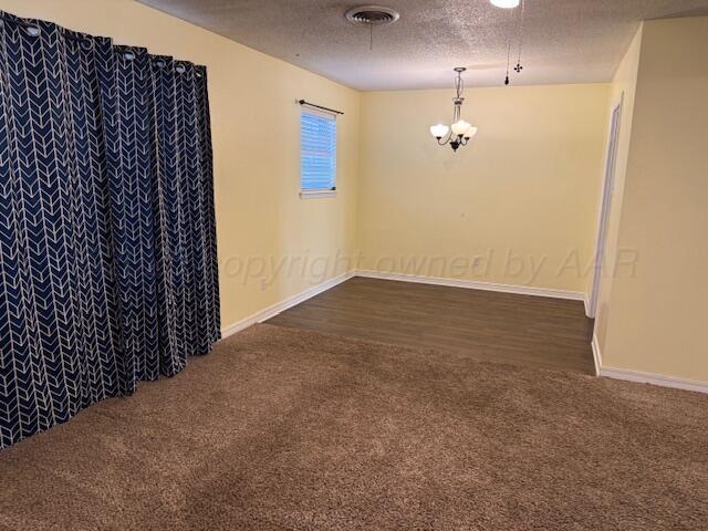 empty room featuring an inviting chandelier, visible vents, dark colored carpet, and a textured ceiling