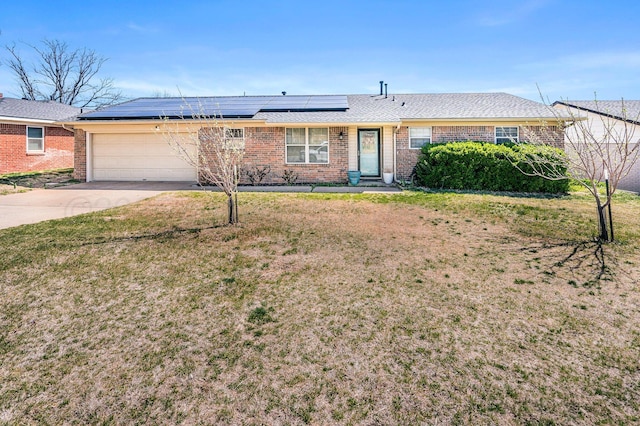 ranch-style house with concrete driveway, an attached garage, a front yard, brick siding, and solar panels