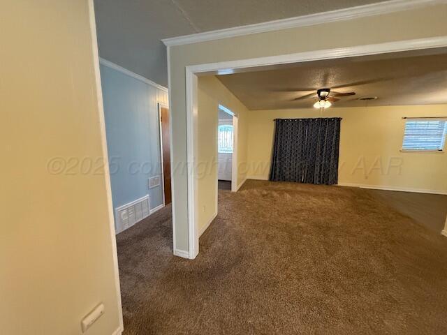 unfurnished living room featuring visible vents, a ceiling fan, dark colored carpet, and ornamental molding