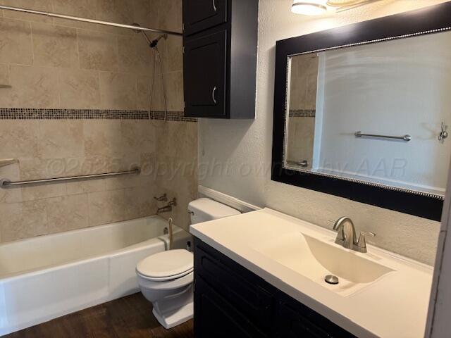 full bathroom featuring vanity, wood finished floors,  shower combination, toilet, and a textured wall