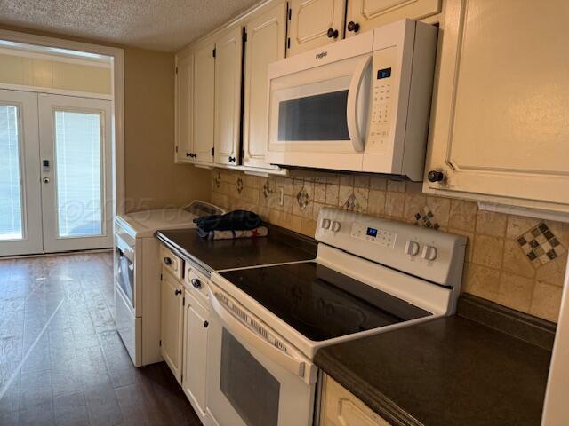 kitchen featuring dark countertops, white appliances, a textured ceiling, and tasteful backsplash