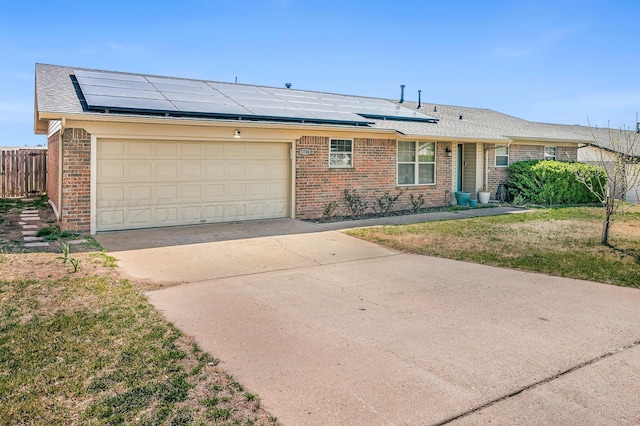 ranch-style home with solar panels, brick siding, and concrete driveway