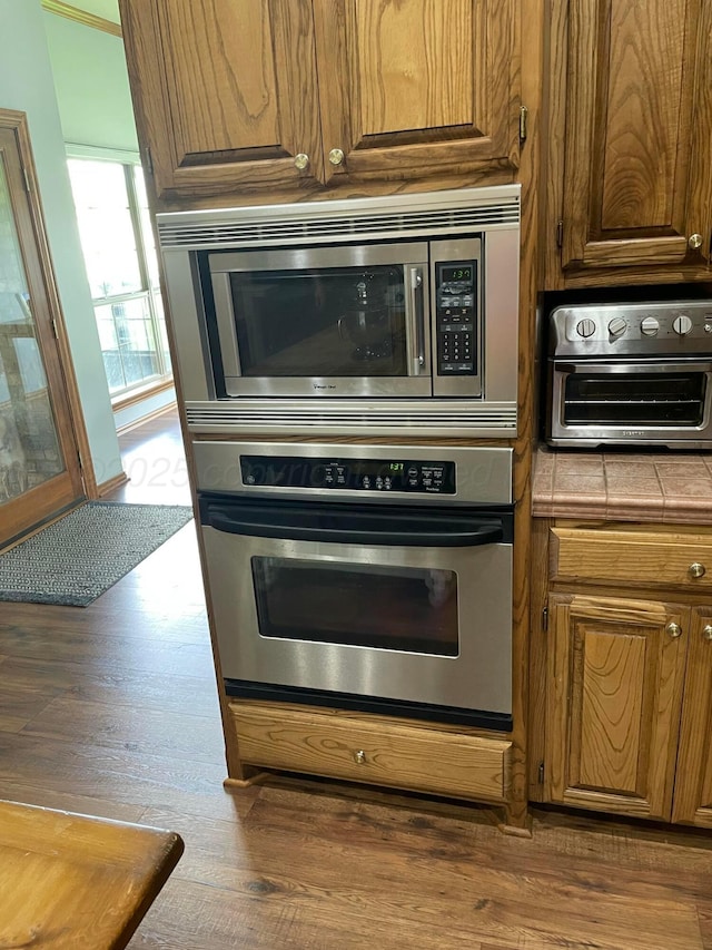 7 Pebble Beach Ct, Amarillo, TX 79124 - kitchen with appliances with stainless steel finishes, tile countertops, dark wood-style flooring, and brown cabinetry